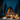 A stunning low-angle shot of a warmly lit A-frame cabin situated in a deep snow-covered forest at night. The cabin's entire front facade is made of glass, glowing with golden light, and is flanked by tall, dark pine trees dusted with snow. Festive Christmas trees adorned with bright golden lights stand prominently in the snow on either side of the cabin's entrance, beneath a clear, star-filled dark blue night sky.