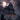 A large, three-story gothic mansion sits amidst a graveyard under a full moon. The house is gray and imposing, with many windows and a covered porch. Gravestones of various shapes and sizes dot the foreground, and a flock of birds flies across the stormy, pink-tinged sky.