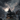 A digitally rendered image shows a three-story gothic mansion on a grassy lot, under a dramatic sky filled with dark clouds and a bright full moon. Gravestones are scattered in front of the house. Silhouetted birds fly through the sky, adding to the ominous and eerie atmosphere.