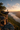 A lone hiker stands silhouetted on a rocky cliff edge, gazing out at a stunning landscape. Below, a valley is partially filled with a thick layer of fog, reflecting the soft colors of the sunrise. The scene evokes a sense of adventure, solitude, and the beauty of nature.