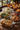 A Thanksgiving dinner is beautifully arranged on a rustic wooden table. The meal includes mashed potatoes topped with herbs, green bean casserole, sliced turkey garnished with thyme, and stuffing in clear glass baking dishes. The warm lighting and autumnal background create a cozy and inviting atmosphere, suggesting a traditional holiday gathering.