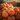 A close-up view shows a large pile of bright orange pumpkins, varying in size and shape. The pumpkins are stacked high, with more pumpkins blurred in the background, creating a sense of abundance. The warm, diffused light highlights the texture of the pumpkins and their stems, evoking a feeling of autumn and harvest.