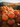 A close-up view shows a large pile of bright orange pumpkins, varying in size and shape. The pumpkins are stacked high, with more pumpkins blurred in the background, creating a sense of abundance. The warm, diffused light highlights the texture of the pumpkins and their stems, evoking a feeling of autumn and harvest.