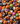 A close-up photograph shows a dense, colorful mix of Halloween candy. The candies include classic candy corn with yellow, orange, and white stripes, orange pumpkin-shaped candies with carved black faces, and round gumball-like candies decorated with various Halloween-themed designs such as eyeballs, ghosts, bats, and monster faces. The candies are tightly packed, filling the entire frame.