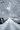 A vertical, eye-level photograph looking down a snow-covered residential street under an overcast sky. Rows of parked cars, completely blanketed in thick white snow, line both sides of the street, which shows a partially cleared, wet, dark grey pavement down the middle. Bare tree branches, also heavily covered in snow, arch overhead, creating a natural tunnel-like effect and framing the peaceful, wintery scene with utility poles and wires visible on the left.