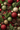 An overhead, full-frame view of a dense Christmas decoration arrangement. The image is filled with green evergreen branches, various red, gold, and lime green spherical ornaments, brown pine cones, and clusters of small red berries. The ornaments feature a mix of glittery, smooth matte, and textured styles, creating a rich and vibrant festive composition.