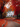 A white two-story house is centered in the image, surrounded by large trees with vibrant red and orange leaves. A pathway covered in fallen leaves leads up to the house. The scene evokes a sense of warmth and autumn serenity.
