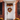 A charming front door decorated for autumn. A white door is centered in the frame, framed by red brick and dark window shutters. A vibrant fall wreath hangs on the door and garland sits above it. Orange and white pumpkins and potted mums decorate the steps leading to the door.