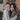 A close-up, vertical shot of two young women with radiant smiles, hugging each other warmly. They are looking directly at the camera, with a blurred, warmly lit Christmas tree visible in the background, creating a festive atmosphere.
