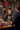 A smiling blonde woman, a shop assistant in a striped apron and dark green sweater, warmly assists a male customer at a wooden counter. The festive shop is decorated with Christmas garlands, red bows, and wrapped gifts, creating a cheerful holiday atmosphere. The woman's genuine smile and the cozy setting evoke a sense of excellent customer service and local retail charm during the holiday season.