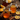 A close-up shot shows two clear mason jar mugs filled with a light orange liquid, likely a hot toddy. The mugs are surrounded by orange slices, cinnamon sticks, star anise, and cloves on a dark, rustic wooden surface. A jar of honey is visible in the blurred background, creating a warm and inviting scene.