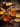 A close-up shot shows two clear mason jar mugs filled with a light orange liquid, likely a hot toddy. The mugs are surrounded by orange slices, cinnamon sticks, star anise, and cloves on a dark, rustic wooden surface. A jar of honey is visible in the blurred background, creating a warm and inviting scene.