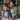 A smiling mother and her young daughter, both wearing matching grey sweaters and snowflake aprons, stand together in a rustic kitchen, hands covered in flour as they knead dough on a wooden table. Soft, warm lighting illuminates their joyful expressions and the cozy, festive background adorned with candles and string lights, capturing a moment of loving family connection during holiday baking.