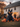 A large, black inflatable cat sits in the front yard of a white farmhouse. Carved pumpkins with lit faces are scattered around the cat and the yard. The farmhouse is decorated with pumpkins and autumn foliage, creating a festive Halloween scene.