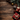 A top-down view of various Christmas decorations and gifts arranged on a dark brown wooden surface with visible grain. The festive arrangement includes red and gold baubles, natural pine cones, several wrapped presents in red and craft paper with ribbons, and green pine branches, all framing an empty central space. The image evokes a warm, festive, and traditional holiday mood, ideal for seasonal greetings.