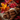 A close-up shot shows a stack of cinnamon sticks tied together with twine sitting on a square piece of burlap material. The cinnamon sticks are dark brown and have visible curls at the ends. Behind the cinnamon sticks, the background is blurred, showing out-of-focus colorful autumn leaves and red berries.