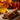 A close-up shot depicts a bundle of brown cinnamon sticks, tied with a natural twine, resting on a square of coarse burlap fabric atop a dark wooden surface. The background features blurred autumn leaves in warm yellow, orange, and red tones. Loose cinnamon powder is subtly scattered beside the burlap.