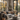 An inviting living room features a gray sofa with tan and brown pillows and a woven throw. A concrete coffee table with a cup and tray sits on a patterned rug. Large windows with black frames offer a view of autumn leaves outside, creating a warm and cozy atmosphere.