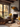 A cozy living room interior with a fireplace and large window showing autumn foliage. Several bouquets of vibrant sunflowers are arranged throughout the room, adding a touch of warmth. A lit fireplace and lanterns create a soft glow, highlighting the natural textures of the room's materials and creating a warm, inviting atmosphere.