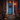 A townhouse doorway decorated for autumn. The weathered blue door is adorned with a colorful wreath and illuminated by a warm lantern. Pumpkins of varying sizes are scattered on the wooden steps leading up to the door, creating a cozy and inviting fall scene.