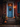 A townhouse doorway decorated for autumn. The weathered blue door is adorned with a colorful wreath and illuminated by a warm lantern. Pumpkins of varying sizes are scattered on the wooden steps leading up to the door, creating a cozy and inviting fall scene.