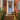 The image shows the front entrance of a brick home decorated for autumn. A weathered light blue door is centered in the frame, adorned with a colorful wreath made of fall leaves and berries. Several orange and white pumpkins of varying sizes, and pots of blooming mums line the brick steps, creating a festive and inviting scene.