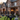 A two-story brick house is heavily decorated for Halloween. A large black spider and a skull with small pumpkins sit on the front lawn. Various ghost-like figures stand on the porch and in the front yard, creating a festive and eerie Halloween scene.
