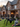 A two-story brick house is heavily decorated for Halloween. A large black spider and a skull with small pumpkins sit on the front lawn. Various ghost-like figures stand on the porch and in the front yard, creating a festive and eerie Halloween scene.