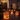 The image shows a nighttime scene of a stately home's walkway adorned with Halloween luminaries. Several paper bags with jack-o'-lantern faces are illuminated from within, casting a warm glow on the stone path. The scene is festive and inviting, perfect for celebrating the Halloween season.