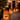 A row of illuminated paper bag luminaries lines a stone walkway leading to a house at night. Each paper bag has a jack-o'-lantern face cut into it and emits a warm orange glow. The house in the background is softly illuminated, creating a festive and welcoming Halloween scene.