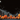 Illustration of a Halloween scene featuring several carved pumpkins with smiling faces lined up in the foreground. Behind the pumpkins are silhouetted haunted houses under a dark night sky with a full moon. Floating ghostly shapes and hand-drawn elements add to the spooky atmosphere.