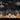 A chalkboard-style illustration depicts a Halloween scene. Several smiling jack-o'-lanterns of varying sizes are lined up in the foreground, with some pumpkins drawn in orange and others in white. Behind them is a row of small houses with simple outlines, set against a black night sky with a crescent moon and fluffy clouds.