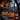A rustic wooden table is adorned with three glowing jack-o'-lanterns of varying sizes and two antique-looking lanterns in a nighttime outdoor setting. A lit candle sits next to one of the lanterns. In the blurred background, lights hang across a wooden house with visible stairs and a wooded area is visible beyond.