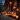 A festive Halloween scene features several carved pumpkins with glowing faces placed on the wooden porch of a log cabin. A lit candle sits inside a vintage-style lantern on the right and smaller lanterns are placed in the background. The warm orange light from the pumpkins and lanterns illuminates the scene against the dark blue sky, creating a cozy and inviting atmosphere.