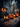 A Halloween scene shows a dark, weathered wooden table with a black, vintage-style lantern on the left holding two lit candles. Next to the lantern are three orange pumpkins with carved, illuminated faces. In the blurred background, there is a building and bokeh lights, creating a spooky and festive atmosphere.