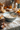 Close-up of a blue bowl filled with flour and a whisk resting inside. Around the bowl, there are cracked eggshells and scattered flour on the countertop. In the background, you can see whole eggs in a carton and small orange and yellow pumpkins along with autumn flowers, all set in a rustic kitchen.