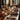A long wooden table is set for a fall dinner, showcasing a festive and elegant atmosphere. Autumn leaves and miniature pumpkins are scattered amongst layered plates, woven placemats, and crystal glassware. Burning candles in ornate holders add a warm glow to the scene, creating a cozy and inviting ambiance.