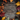 A detailed overhead view displays a rustic wooden surface framed by a rich assortment of autumn elements. Colorful leaves in shades of deep red, orange, yellow, and muted green are interspersed with dark brown pinecones and light brown acorns with caps. The natural arrangement creates an irregular border around the textured wooden planks, offering a warm and inviting autumnal backdrop.
