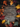 A detailed overhead view displays a rustic wooden surface framed by a rich assortment of autumn elements. Colorful leaves in shades of deep red, orange, yellow, and muted green are interspersed with dark brown pinecones and light brown acorns with caps. The natural arrangement creates an irregular border around the textured wooden planks, offering a warm and inviting autumnal backdrop.