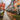 A vibrant street scene depicting a long row of modern townhouses on an overcast autumn day. The wet concrete sidewalk is covered with countless fallen red, orange, and yellow leaves, mirroring the bright foliage of a large tree in the foreground. The houses themselves are painted in various striking colors, including red, orange, grey, and yellow, each with front steps and black railings, adding a lively contrast to the muted sky and wet ground.