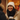 A young biracial woman with long dark hair smiles widely, revealing her dimples and teeth, as she looks towards someone off-camera. She is bundled in a cream knitted beanie and a beige puffer jacket, holding a white disposable coffee cup with black gloved hands, standing outdoors in what appears to be a snowy urban environment with blurry warm lights in the background.