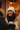 A young biracial woman with long dark hair smiles widely, revealing her dimples and teeth, as she looks towards someone off-camera. She is bundled in a cream knitted beanie and a beige puffer jacket, holding a white disposable coffee cup with black gloved hands, standing outdoors in what appears to be a snowy urban environment with blurry warm lights in the background.