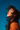 A close-up, profile shot of a young woman with dark, wind-swept hair looking upwards with her eyes closed against a vibrant blue sky. Her skin is illuminated by warm sunlight, appearing dewy and radiant, and she wears a bright orange top. The image evokes a strong sense of peace and natural joy.