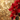 A vibrant red poinsettia plant is positioned on the right side of the frame, with its large crimson bracts lightly dusted with white specks, possibly glitter. Small green leaves and buds are visible among the red foliage. The background is a soft, blurry golden bokeh, featuring numerous circular light blurs of varying sizes, creating a warm and festive glow.
