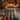 A low-angle shot depicts two pairs of legs, clad in intricately patterned knitted socks (one pair orange and grey, the other cream and brown), resting on a white faux fur rug. In the softly blurred background, a warm fire crackles in a rustic stone fireplace, flanked by stacked logs and illuminated by numerous flickering candles and warm string lights, creating an inviting and tranquil ambiance.