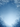 A serene vertical image of a winter scene with snow falling against a gradient blue sky. Bare tree branches, heavily coated in white snow and frost, frame the top and bottom edges of the image, creating a natural archway. The sky transitions from a darker blue at the top to a lighter, almost white blue at the bottom center, with numerous small white snowflakes gently descending across the entire frame.