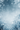 A vertical image depicting a serene winter scene. The top and sides are framed by large, intricate white snowflakes, while a soft snowfall of smaller white specks fills the ethereal blue gradient background. Frosted, bare tree branches covered in ice and snow are visible along the bottom edge, creating a peaceful and magical winter wonderland ambiance.