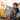 A close-up shot of a smiling African American father with his young, curly-haired mixed-race son on his shoulders. Both are looking joyfully off-camera towards the right, bathed in warm golden sunlight that highlights their faces and the child's luminous curls, set against a softly blurred background of a house and glowing autumn trees, conveying a loving family moment.