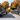 A scenic view of a quiet main street in a small town during autumn. The street is lined with historic red brick buildings housing shops, and large trees with vibrant golden and orange fall foliage. Several cars are parked along both sides of the road, and an American flag hangs from a black lamppost on the right, under a clear blue sky.