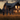 A family of four, consisting of two adults and two young children, walks away from the viewer through a vibrant golden field of tall grass towards a cozy, dark wooden house. The house's windows glow warmly with interior light, contrasting with the deep blues and oranges of the twilight sky, while the family's silhouettes are softly illuminated by the last rays of the setting sun, evoking a profound sense of peace and belonging at home.
